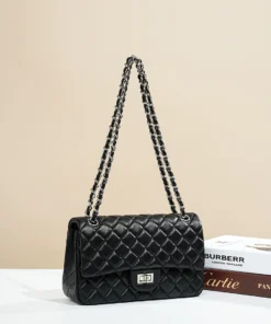A luxurious black quilted chain bag with silver hardware and a classic turn-lock closure, displayed next to designer books.