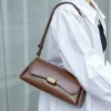 A woman in a white shirt carrying a smooth brown cowhide clasp bag, highlighting its elegant, textured gold clasp.