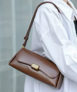 A woman in a white shirt carrying a smooth brown cowhide clasp bag, highlighting its elegant, textured gold clasp.