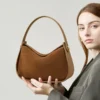 Brown Suede Handbag — curved hobo shoulder bag with short top handle and gold hardware on a light grey background